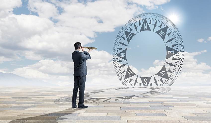 A businessman stands in a large open area as he uses a spyglass to view a compass that sits on the horizon in the distance.